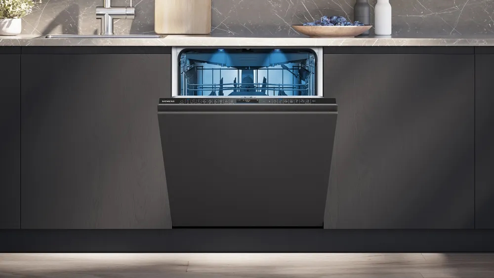 The Siemens dishwasher integrated into dark kitchen cabinetry with the door slightly ajar and blue interior lighting.