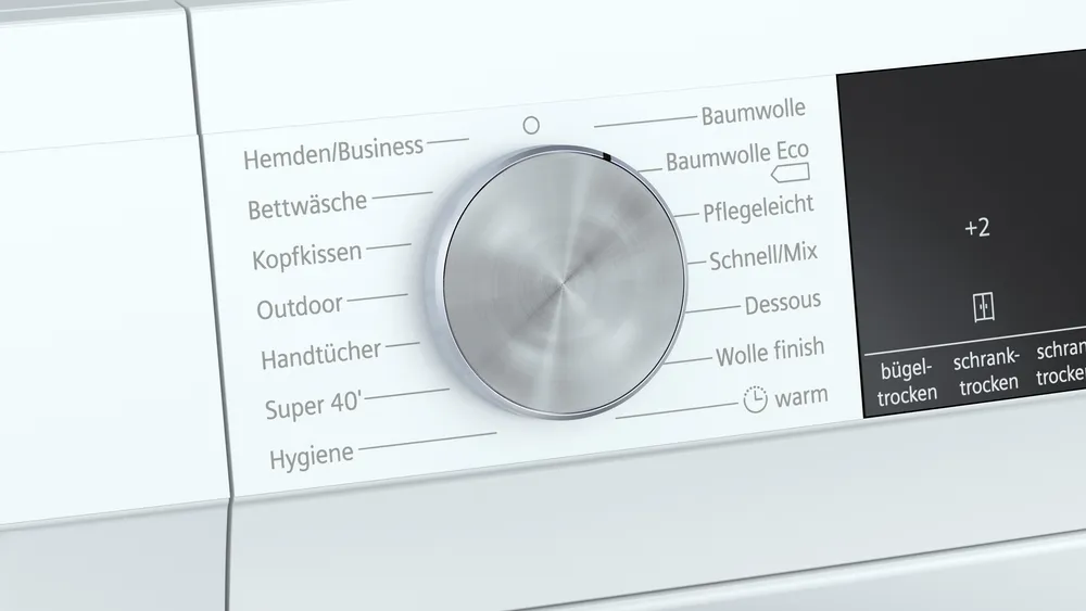 Close-up of the silver program selector dial of the dryer, showing programs like Cotton Eco, Outdoor, and Hygiene.
