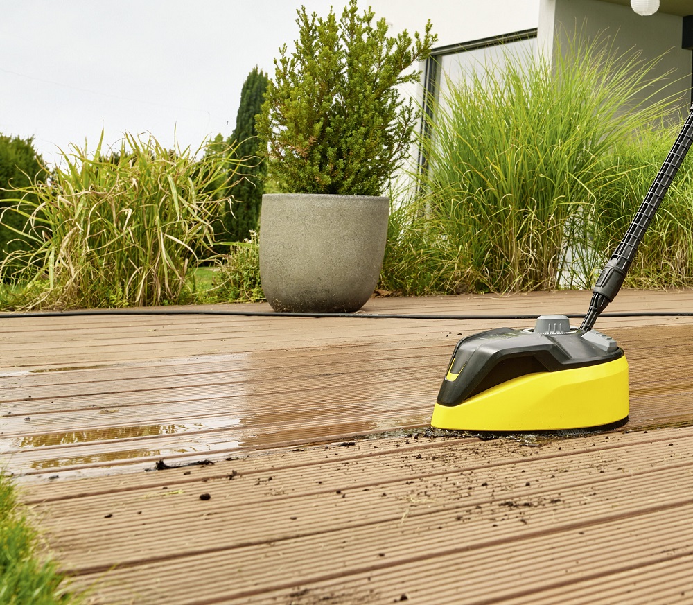 The yellow and black T-Racer surface cleaner in use on wooden decking, effectively cleaning dirt and mud.