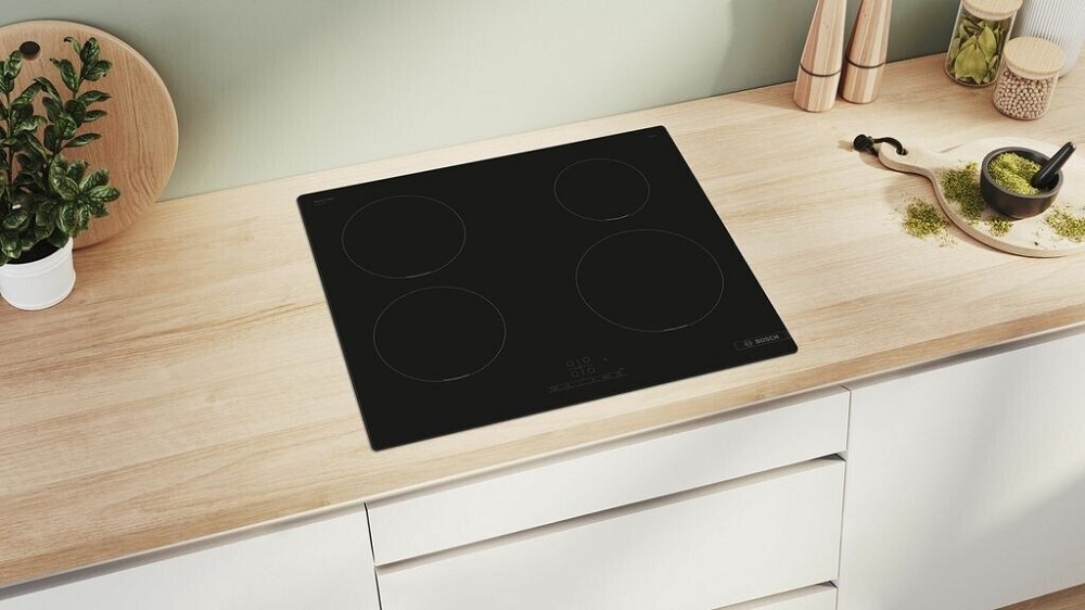 The Bosch induction hob in a modern kitchen, embedded in a light wooden countertop, surrounded by decor.