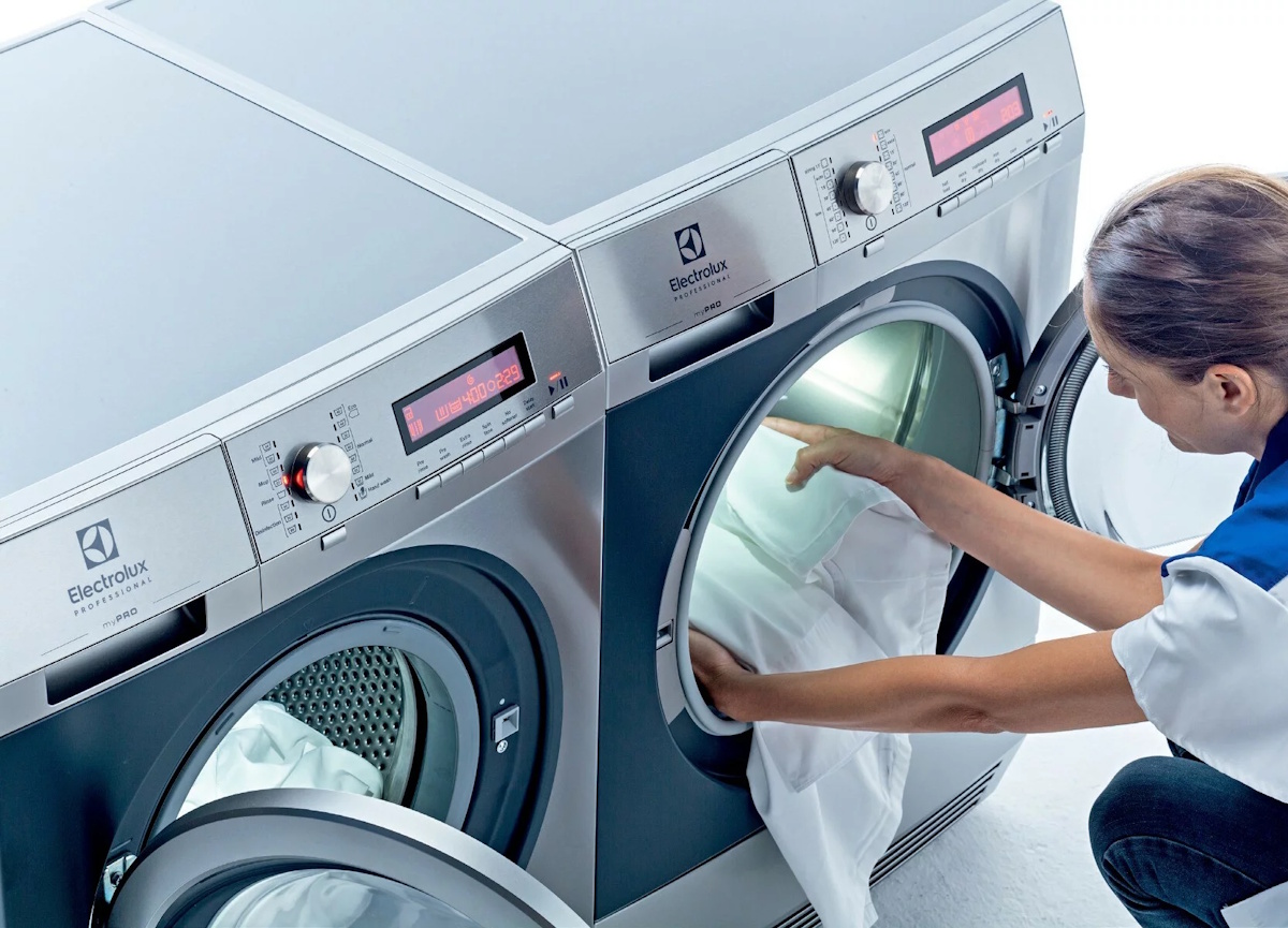 A person loading bulky textiles through the large door opening into the illuminated drum of the Electrolux machine.