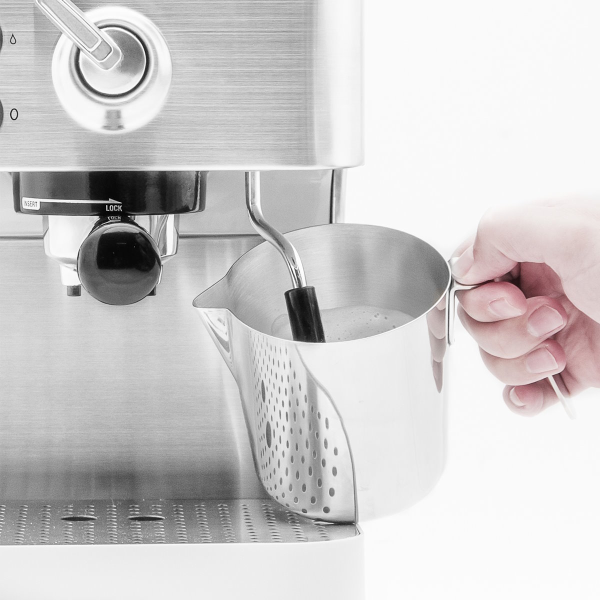 Close-up: The steam wand of the Gastroback espresso machine frothing milk in a perforated stainless steel milk jug.
