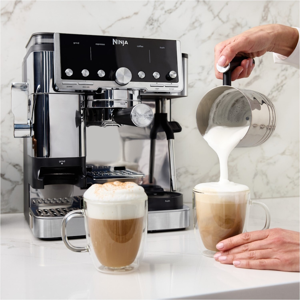 The NINJA ES701EU espresso machine in the background while milk foam is poured into a cappuccino glass